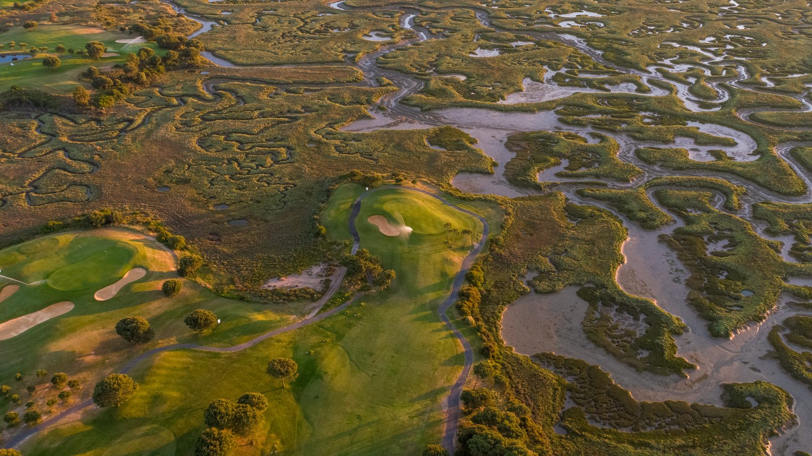 Aerial view of a golf green surrounded by tidal marshland channels at El Rompido